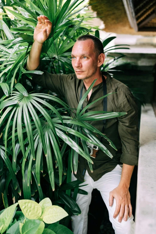 a man standing next to a lush green plant, john waters, conde nast traveler photo, profile image, avatar image