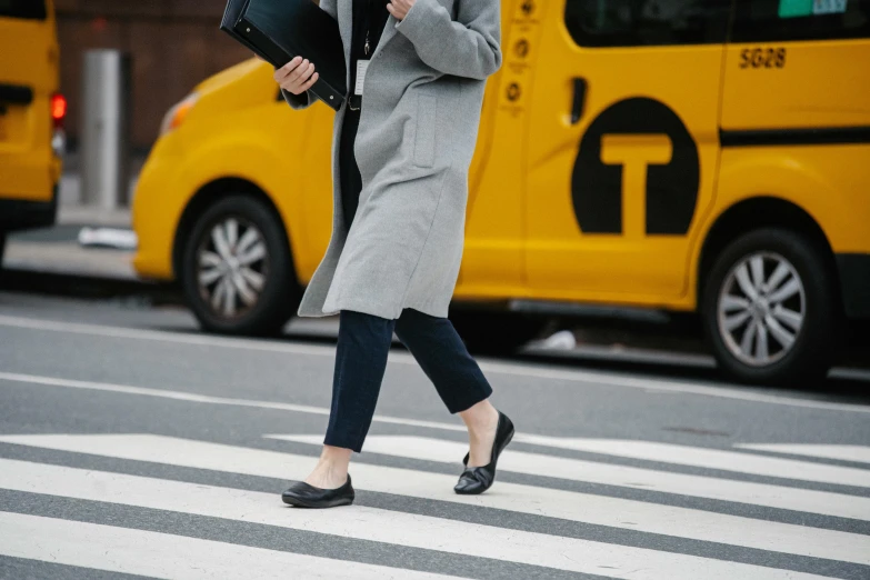 a woman walking across a street while holding an umbrella, by Nina Hamnett, trending on unsplash, yellow and charcoal leather, black loafers, grey turtleneck coat, work clothes