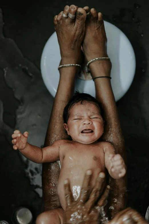 a close up of a person holding a baby, by Elsa Bleda, pexels contest winner, renaissance, bleeding in the bath, bali, holding his hands up to his face, spinning hands and feet