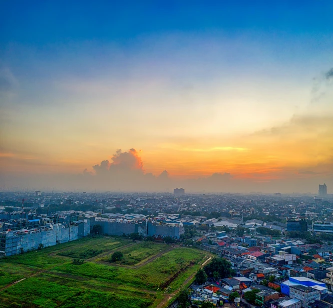 an aerial view of a city at sunset, pexels contest winner, sumatraism, grass field surrounding the city, orange and blue sky, high quality upload, colorfull sky