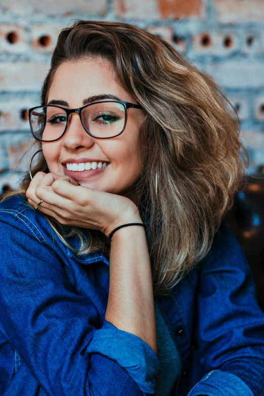 a woman with glasses sitting in front of a brick wall, trending on pexels, flirting smiling, square glasses, pokimane, half image