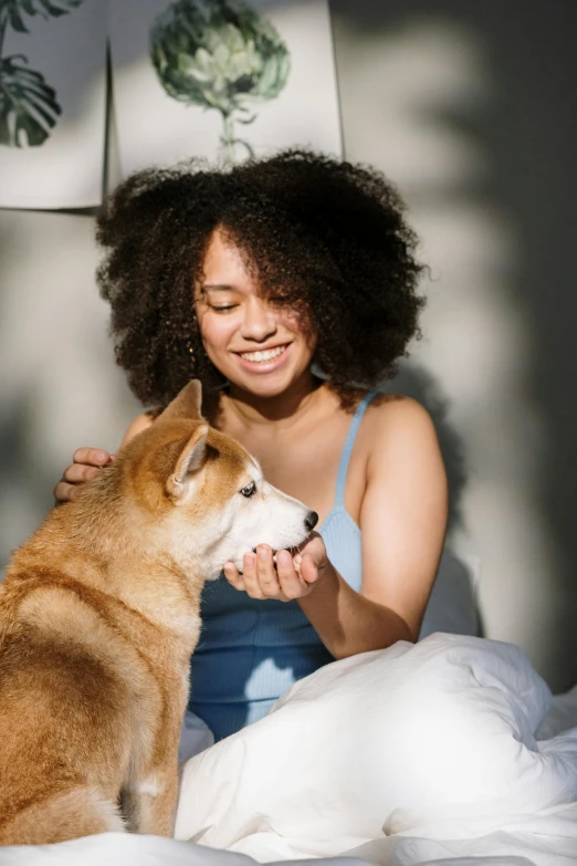 a woman sitting on a bed petting a dog, a stock photo, trending on pexels, renaissance, mixed-race woman, shibu inu, snacks, a still of a happy