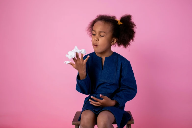 a little girl sitting on top of a wooden chair, wearing nanotech honeycomb robe, navy shirt, picking up a flower, bumpy nose