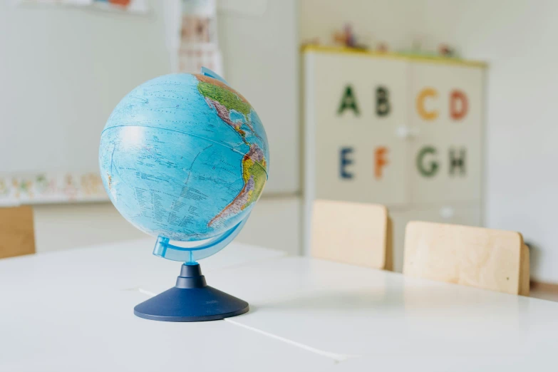 a blue globe sitting on top of a white table, in a school classroom, detailed product image, from the front, medium-shot