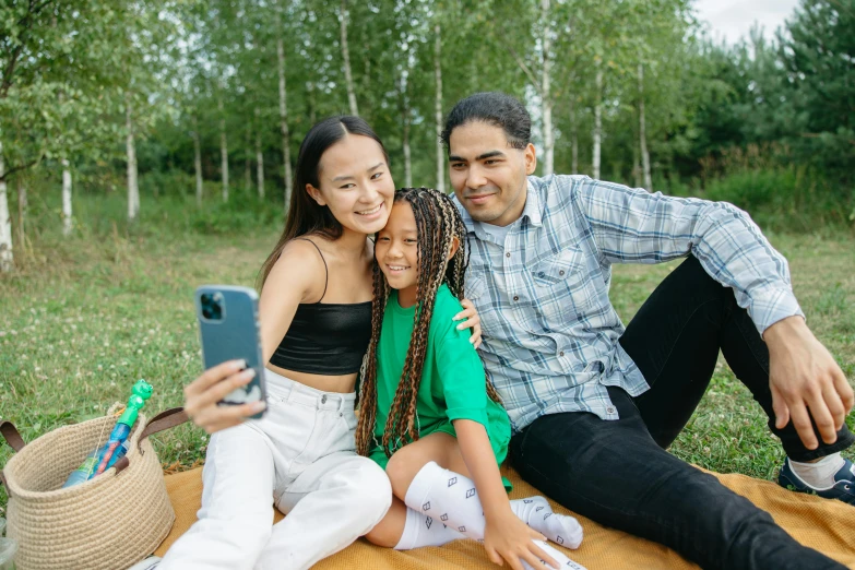 a couple of people sitting on top of a blanket, a picture, cellphone, of a family standing in a park, light skin, gen z