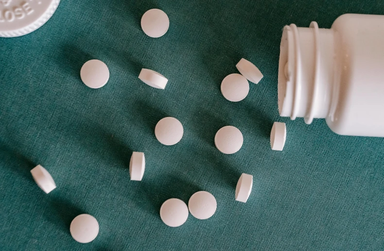 a close up of a bottle of pills on a table, a picture, by Emma Andijewska, unsplash, plasticien, white and teal garment, circle forms, set pieces