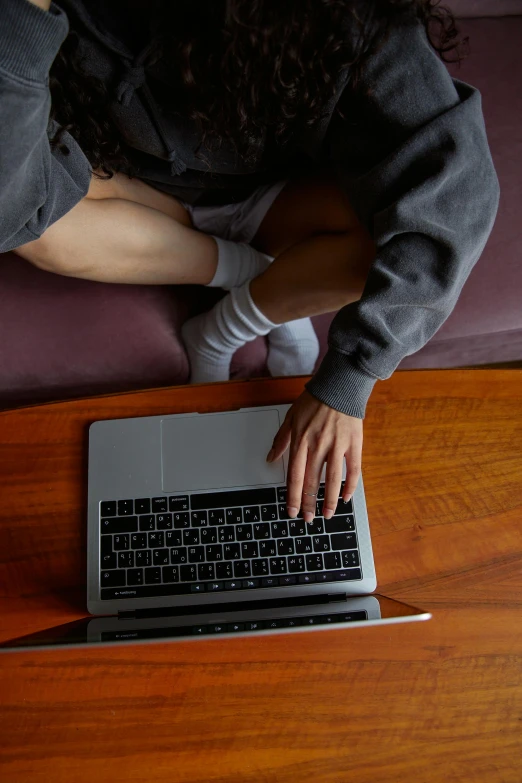 a woman sitting on a couch using a laptop, by Carey Morris, pexels, gray shorts and black socks, wearing jeans and a black hoodie, hands straight down, college