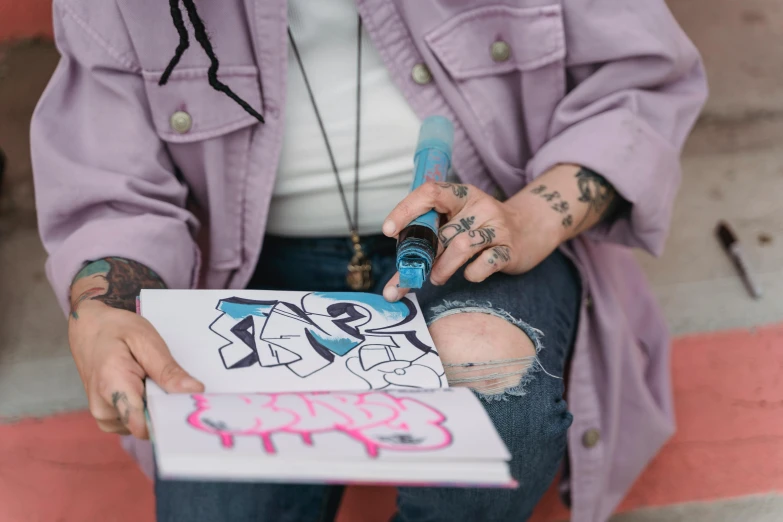 a person that is sitting down with a book, a drawing, pexels contest winner, graffiti, blue ink pen, some purple and blue, streetwear, tattoo artist