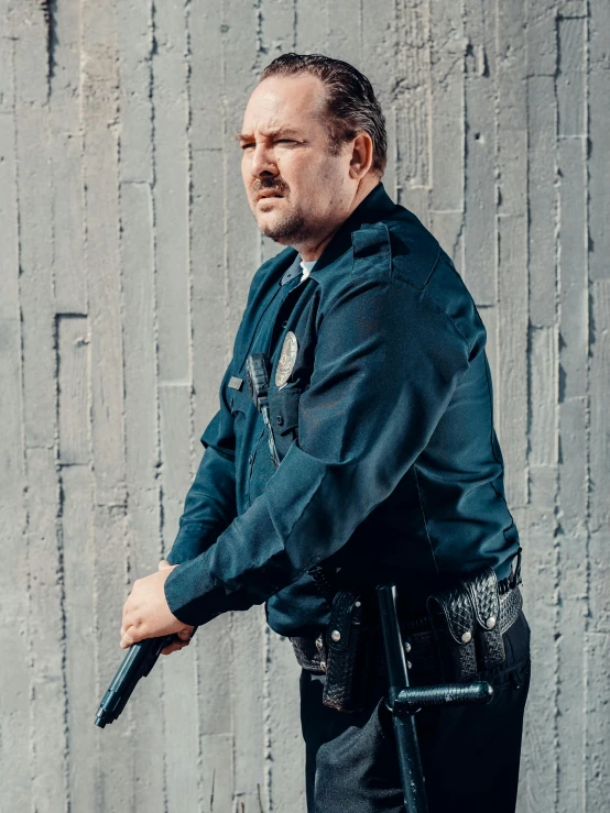 a man in a police uniform holding a gun, by Andrew Stevovich, portrait image, action bronson, cinematic outfit photo, portrait of ricky gervais