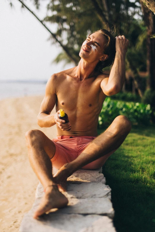 a shirtless man sitting on the side of a beach, holding hot sauce, silicone skin, in an action pose, wide forehead