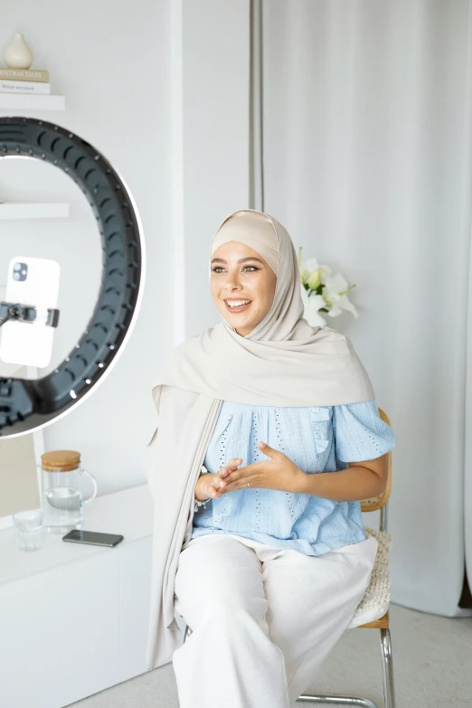 a woman sitting on a chair in front of a mirror, inspired by Nazmi Ziya Güran, featured on instagram, hurufiyya, ring light, on a white table, front camera, halo over her head