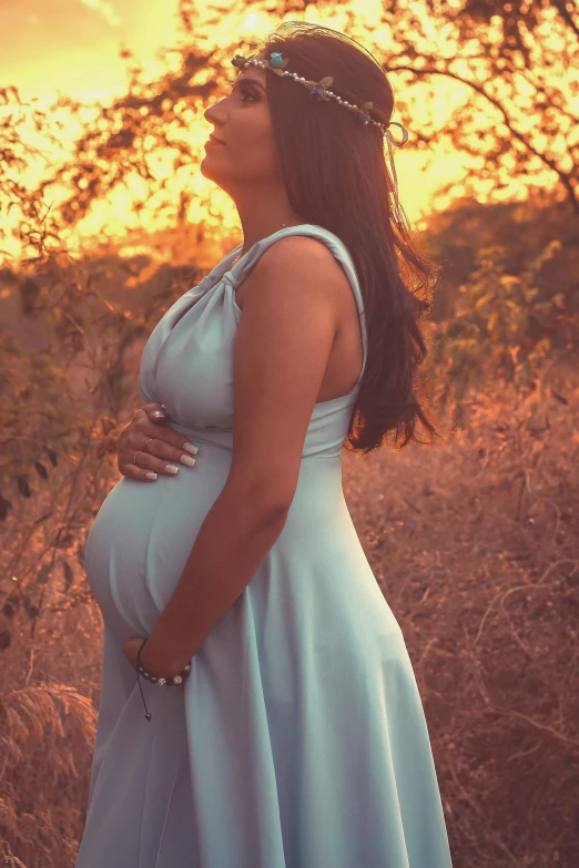 a pregnant woman standing in a field at sunset, an album cover, pexels contest winner, symbolism, wearing blue dress, profile image, perfectly shaded body, alanis guillen