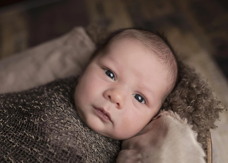 a close up of a baby wrapped in a blanket, brown, colour portrait photograph, rustic, grey