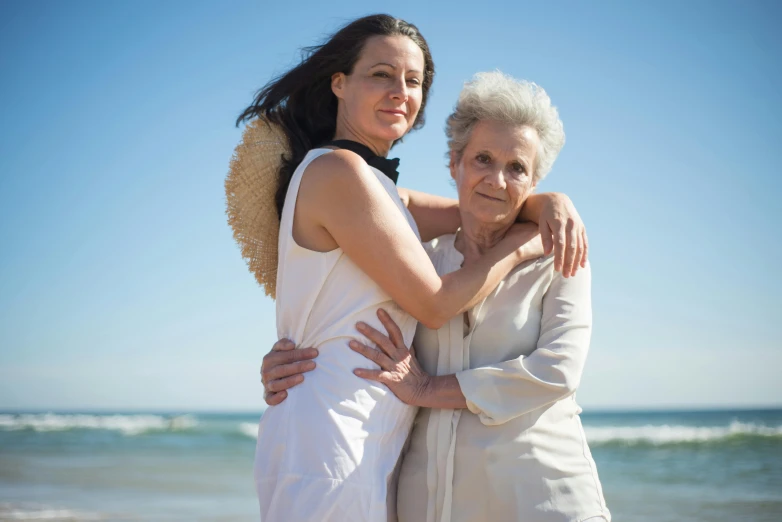 a couple of women standing next to each other on a beach, a portrait, pixabay contest winner, renaissance, sweet hugs, old and young, 15081959 21121991 01012000 4k, nursing