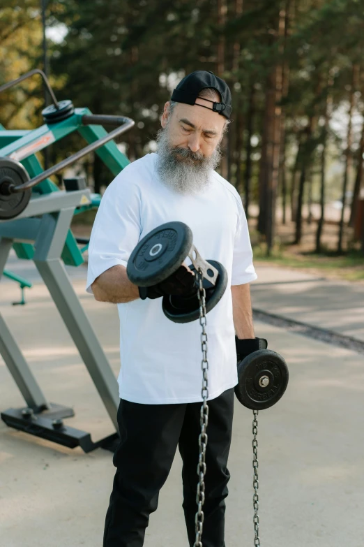 a man with a beard is holding two dumbbells, by Adam Marczyński, pexels contest winner, long white beard, large chain, at the park, gym