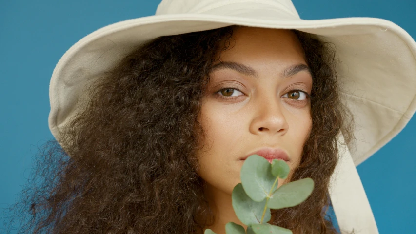 a close up of a person wearing a hat and holding a plant, trending on pexels, renaissance, no makeup wavy hair, mixed-race woman, ad image, charli bowater