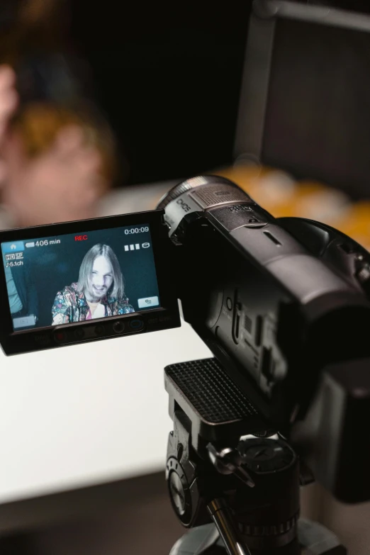 a video camera sitting on top of a tripod, close up to the screen, she is facing the camera, giving an interview, modelling