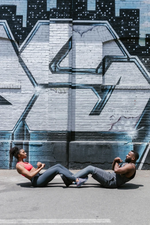 two people sitting on the ground in front of a graffiti wall, chiseled abs, working out, back arched, wakanda