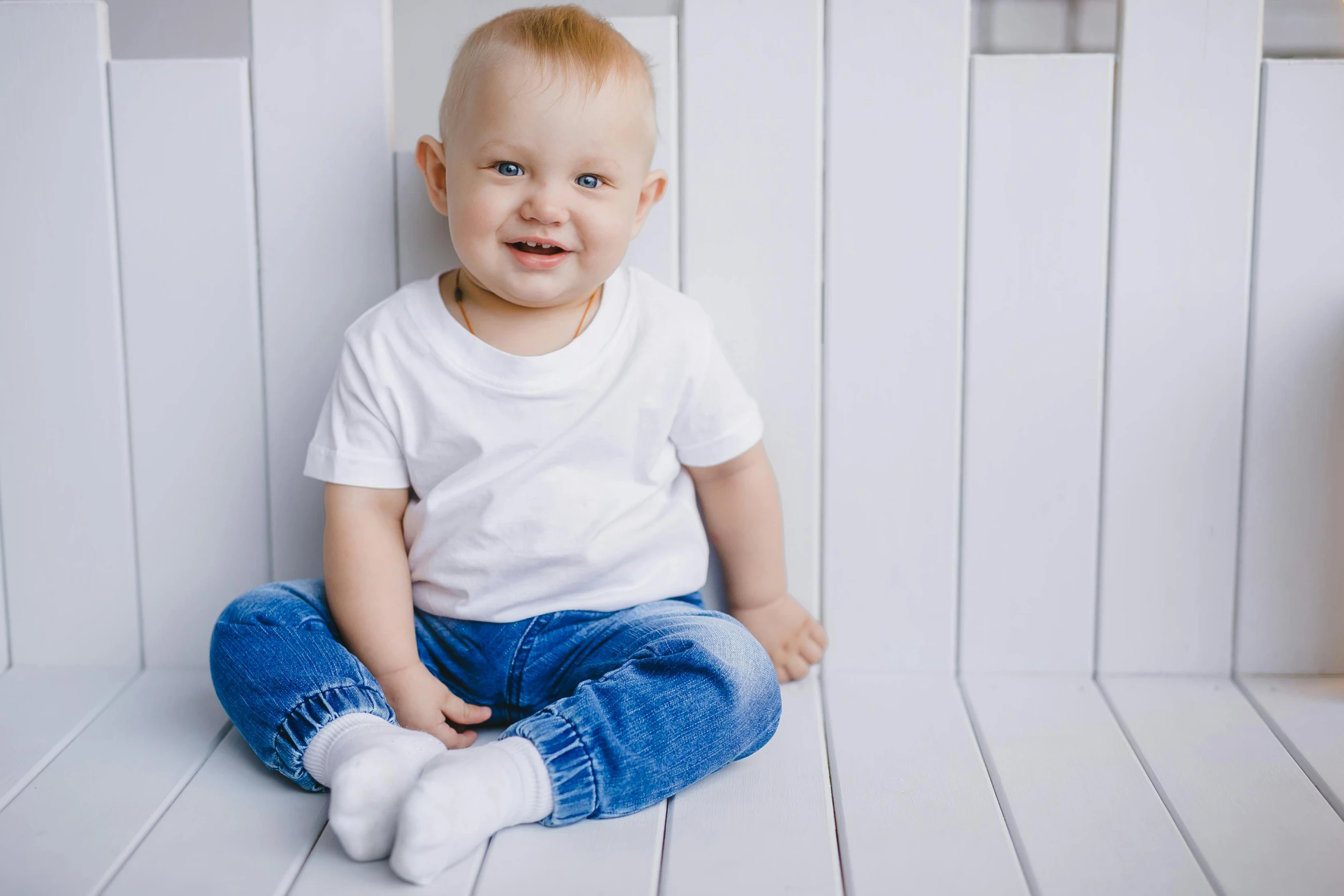 a baby sitting on top of a wooden floor, white shirt and blue jeans, slightly smiling, panels, colour corrected