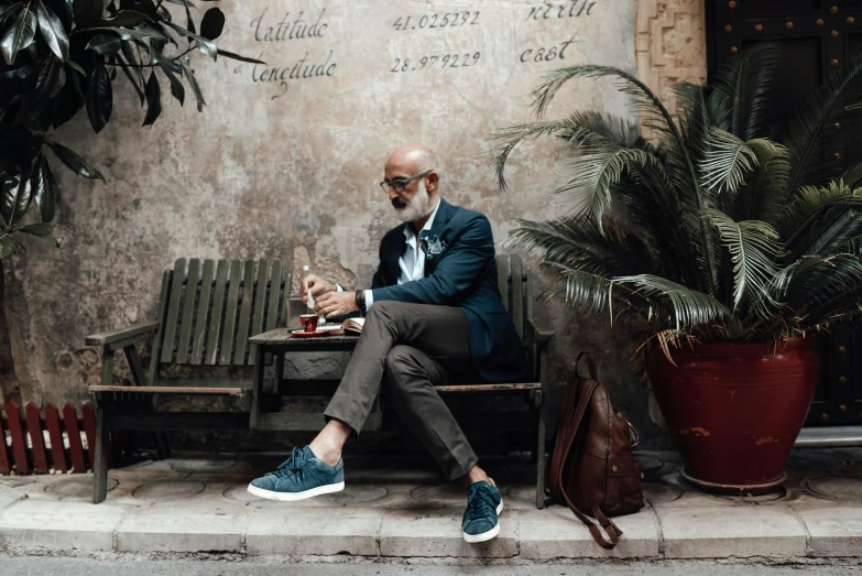 a man sitting on a bench in front of a building, a portrait, by Matija Jama, pexels contest winner, blue shoes, samuel l jackson posing in cafe, : 5 stylish, navid negahban