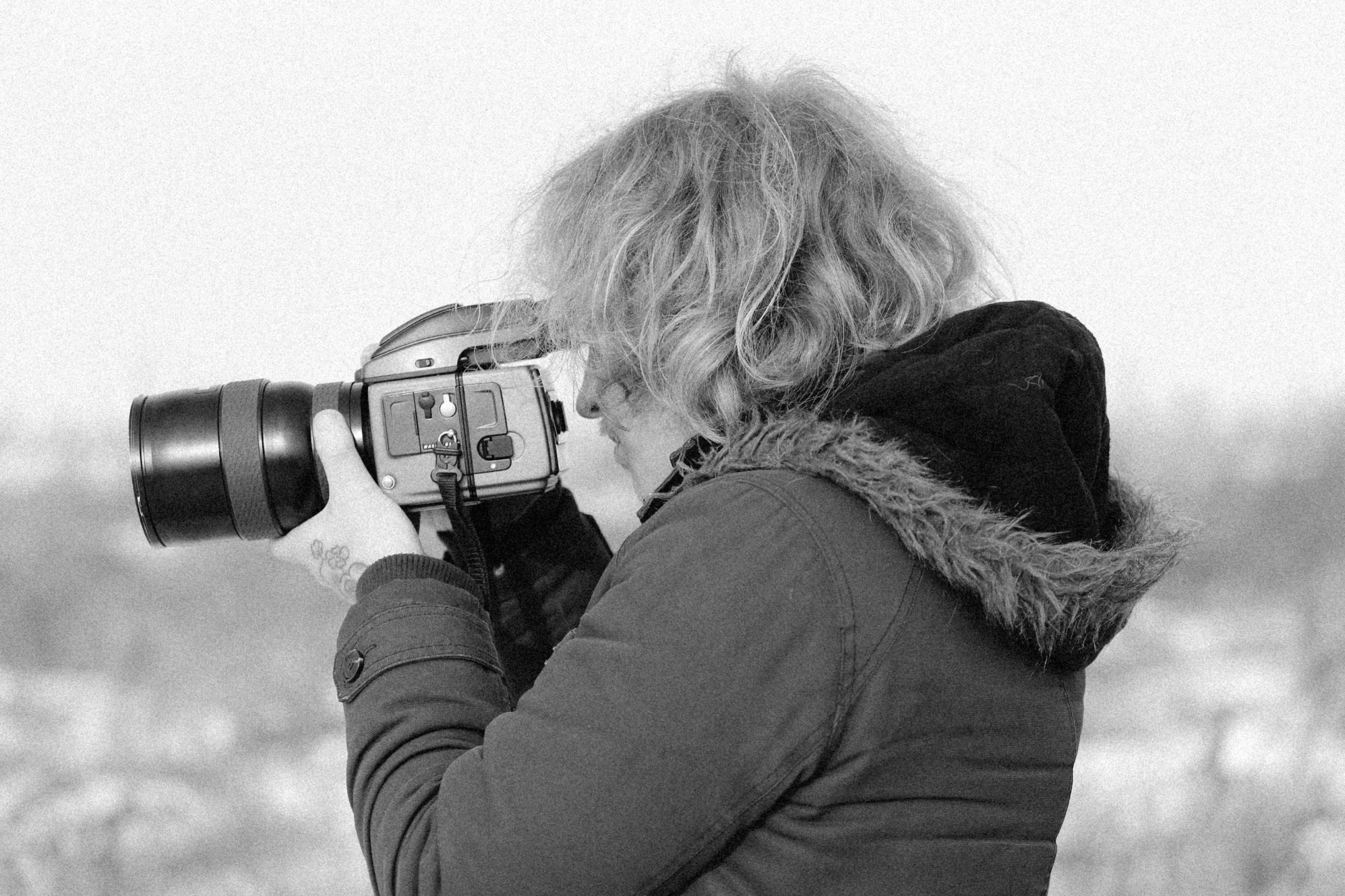 a woman taking a picture with a camera, a black and white photo, inspired by Bert Hardy, pixabay, profile image, medium format, 1980s photography, telephoto