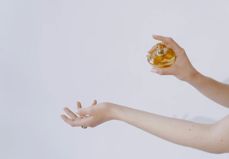 a woman holding a bottle of perfume in her hand, by Gavin Hamilton, trending on pexels, visual art, background image, white and gold, hand gesture, manuka