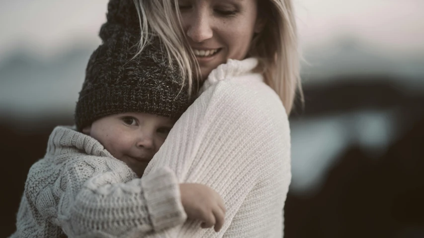 a woman holding a baby in her arms, pexels contest winner, wearing beanie, soft render, blonde, thumbnail