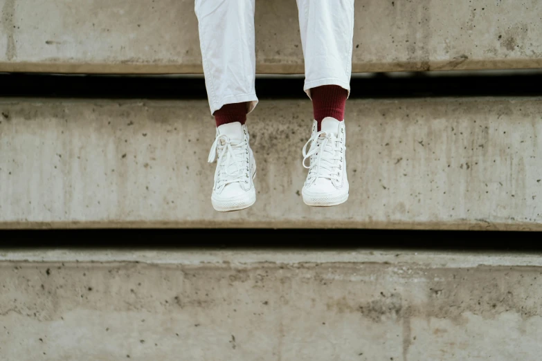 a person that is sitting on some steps, white shoes, from below, maroon and white, white clothing