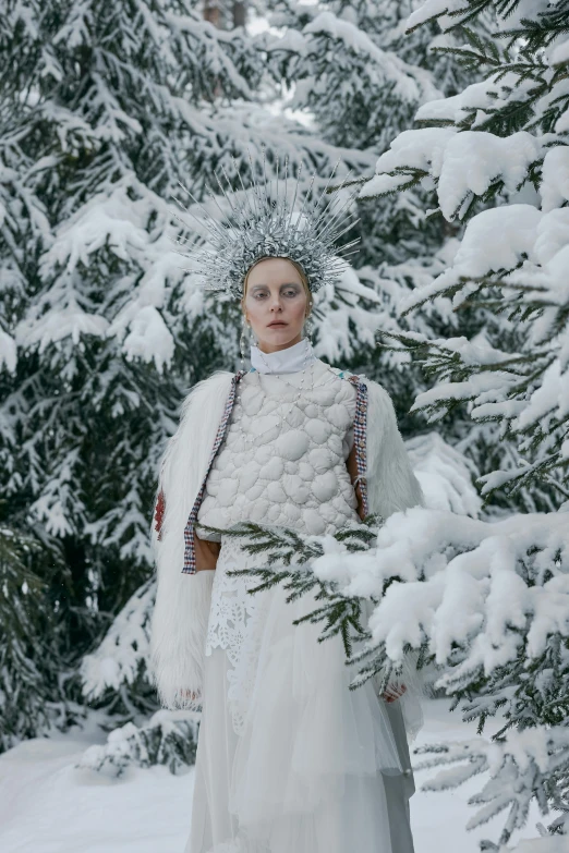 a woman in a white dress is standing in the snow, an album cover, inspired by Louisa Matthíasdóttir, pexels contest winner, renaissance, intricate chrome headdress, bright nordic forest, photo from vogue magazine, from the grand budapest hotel