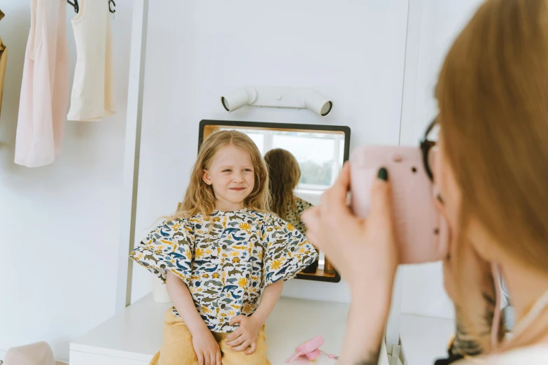 a woman taking a picture of a little girl in a mirror, on a canva, wearing a cute top, avatar image
