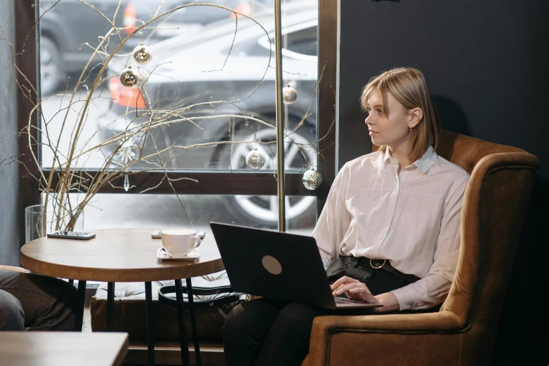 a man and a woman sitting at a table with a laptop, by Emma Andijewska, trending on unsplash, female in office dress, sitting alone in a cafe, sydney hanson, sitting on an armchair