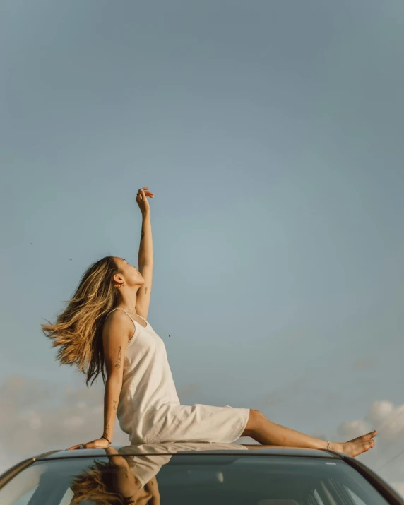 a woman in a white dress sitting on top of a car, pexels contest winner, happening, raising an arm, soaring, slightly minimal, meditation pose
