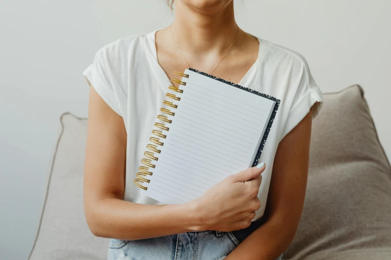 a woman sitting on a couch holding a notebook, by Julia Pishtar, trending on pexels, private press, black marble and gold, white background, lined in cotton, pictured from the shoulders up