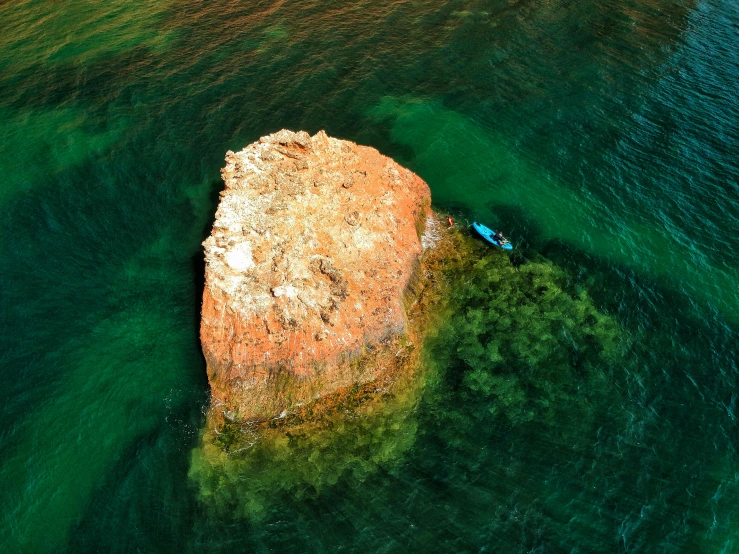 a large rock in the middle of a body of water, by Adam Marczyński, unsplash contest winner, a green, aerial, sup, manly