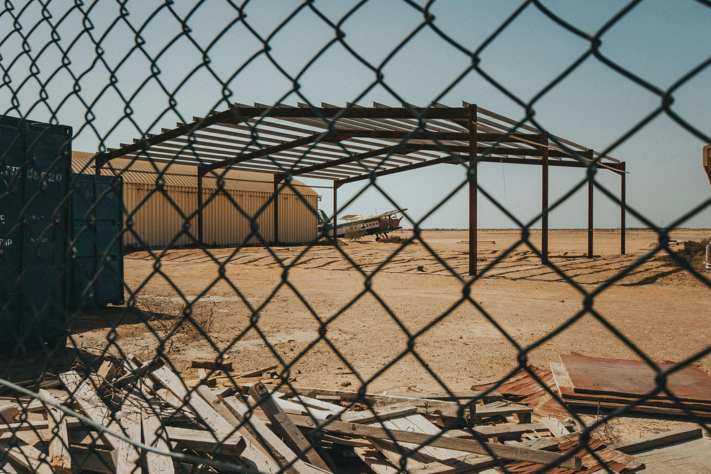 a construction site behind a chain link fence, by Lee Loughridge, pexels contest winner, abandoned in a desert, airplane hanger background, debris on ground, unsplash photography