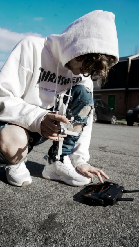 a person kneeling on the ground with a cell phone, an album cover, unsplash, graffiti, white clothing, tri - gun, offwhite, sneaker photo