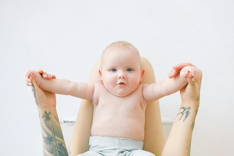 a woman holding a baby in a high chair, pexels contest winner, symbolism, laying down with wrists together, tattooed, looking up at camera, pale bluish skin