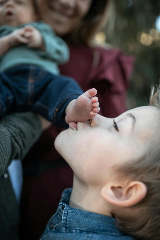 a close up of a person holding a baby, by Jan Tengnagel, unsplash, neck zoomed in from lips down, focus on his foot, outdoor photo, families playing