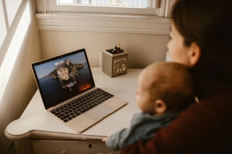 a woman holding a baby in front of a laptop, a picture, by Julia Pishtar, pexels contest winner, video art, in meeting together, high quality product image”, looking outside, long distance photo