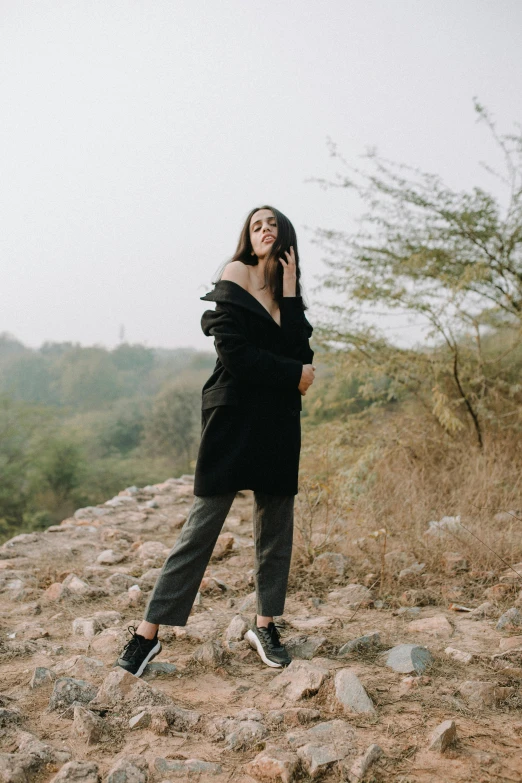a woman standing on top of a rocky hill, a picture, trending on pexels, jet black tuffe coat, young himalayan woman, fullbody photo, casual clothing style