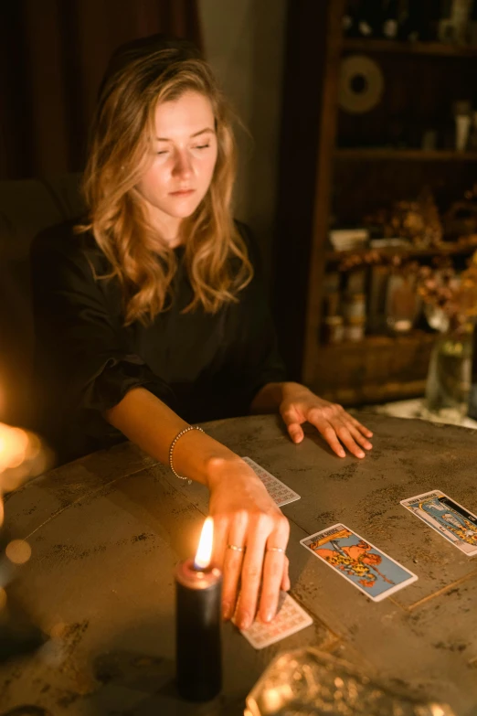 a woman sitting at a table with a candle and playing cards, a portrait, by Julia Pishtar, trending on pexels, casting a protection spell, board games on a table, sydney hanson, 15081959 21121991 01012000 4k