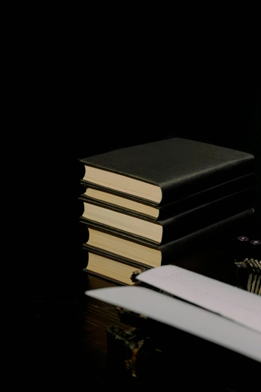 a stack of books sitting on top of a wooden table, on black paper, matte black paper, carefully crafted, on a desk