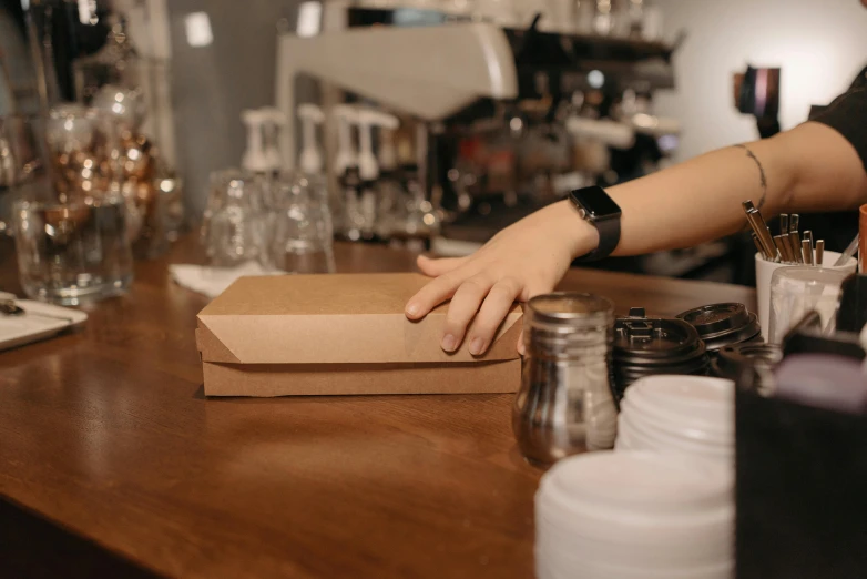 a person standing at a counter with a box on it, pexels contest winner, aussie baristas, parchment paper, thumbnail, hand made