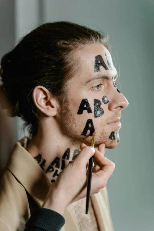 a man with letters painted on his face, by Julia Pishtar, trending on pexels, art & language, synthetic bio skin, letter a, square masculine jaw, behind the scenes photo