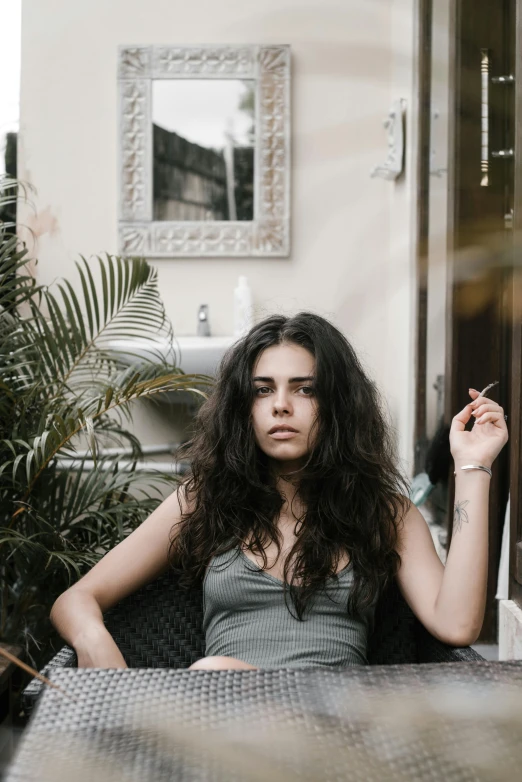 a woman sitting at a table with a cigarette in her hand, an album cover, inspired by Elsa Bleda, pexels contest winner, messy hair bedhead, sitting in the garden, young middle eastern woman, cynthwave