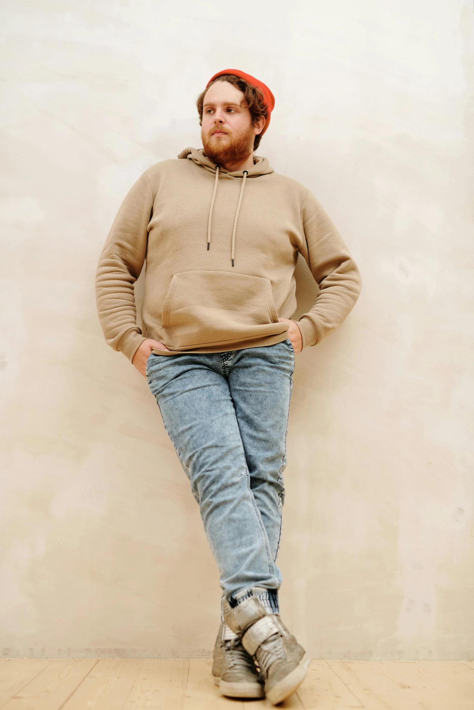 a man leaning against a wall with his hands on his hips, trending on pexels, beige hoodie, jonah hill, jeans and boots, catalog photo
