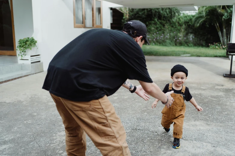 a man standing next to a little boy on a skateboard, pexels contest winner, wearing a backwards baseball cap, expressing joy, pants, black