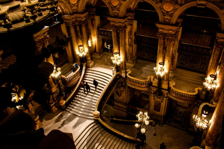 a couple of people walking down a set of stairs, by Daniel Seghers, pexels contest winner, opera, chandeliers, buildings carved out of stone, lit from above