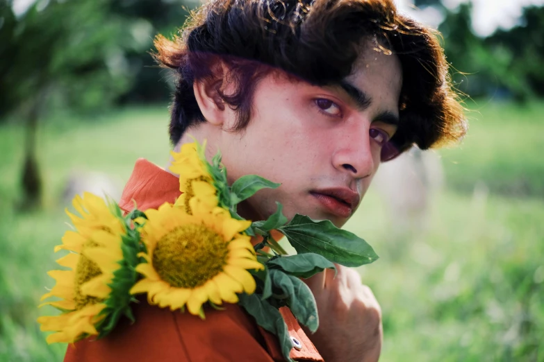 a man with a bunch of sunflowers around his neck, an album cover, trending on pexels, delicate androgynous prince, asher duran, orange hue, lush flora