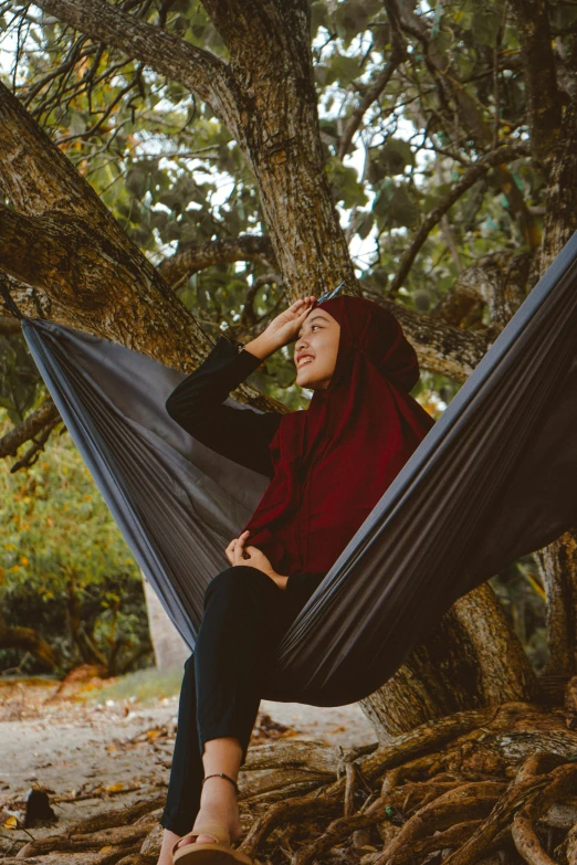 a woman sitting in a hammock under a tree, pexels contest winner, renaissance, wearing a head scarf, dark red, hijab, grey